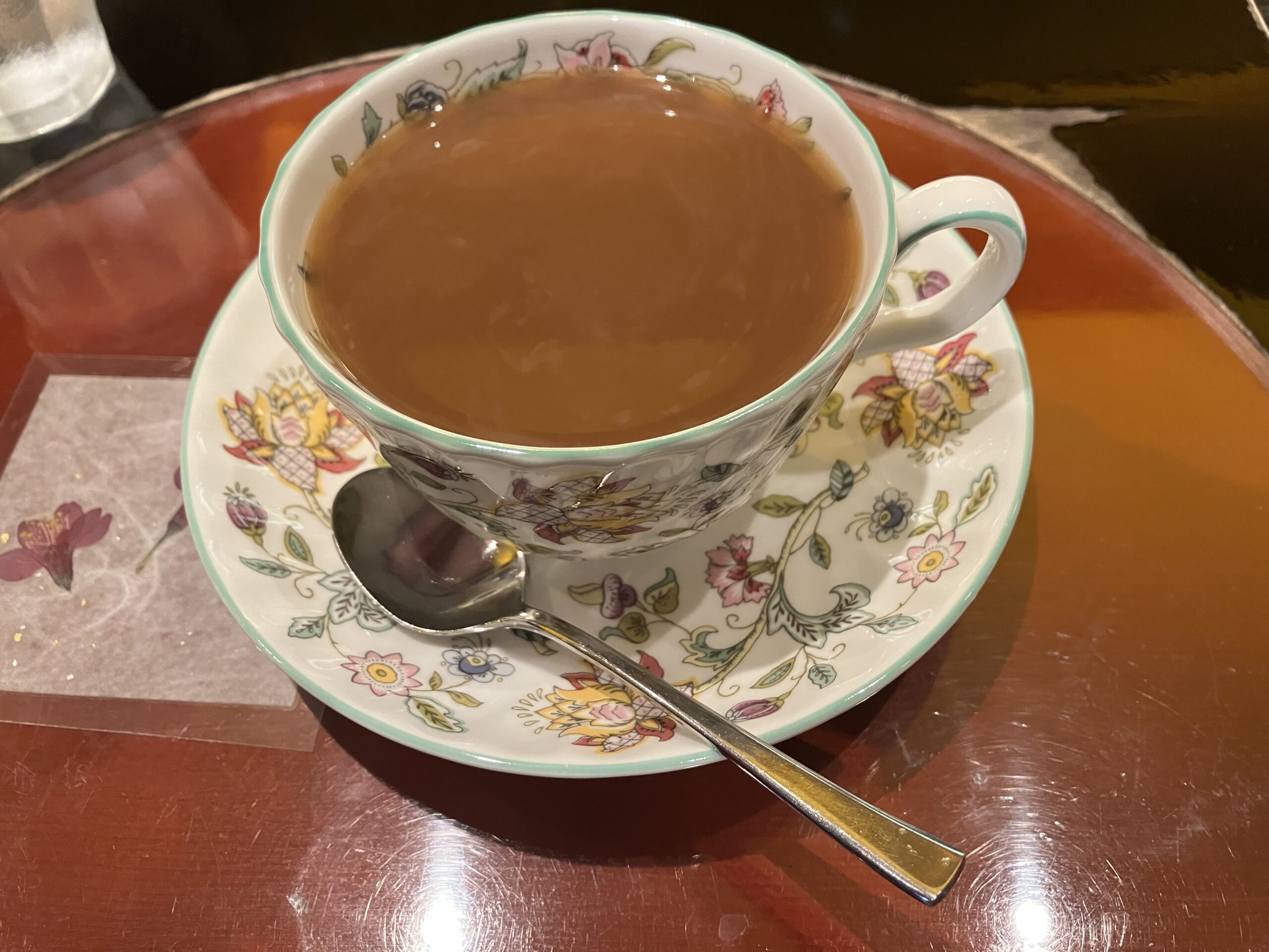 カップに入ったコーヒーの写真。コーヒーには大さじ１杯くらいのミルクがかかっている。カップは色とりどりの花が咲いている絵柄が描かれている。